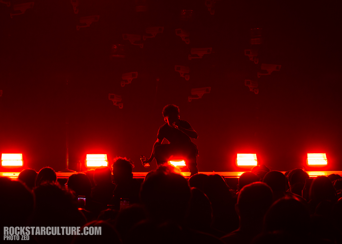 A performer on stage silhouetted against red lights, interacting with the audience during a concert.