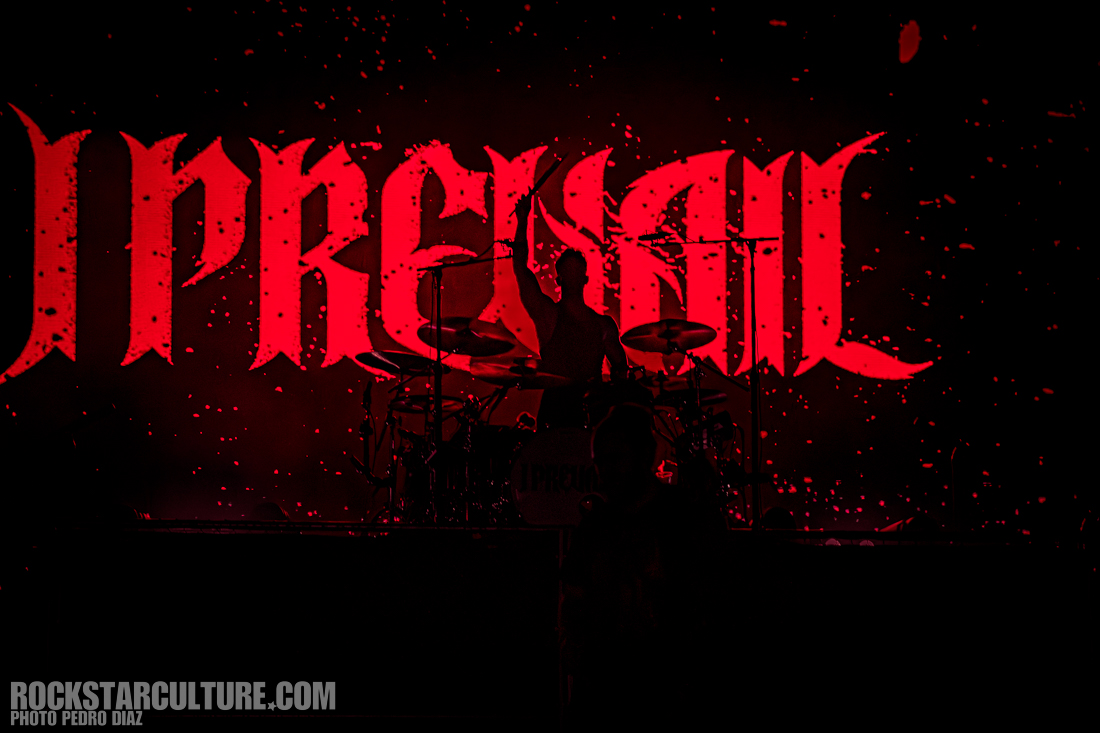 A drummer silhouetted against a large red backdrop displaying the word 'Prevail' in bold letters, with confetti or sparks scattered in the air.
