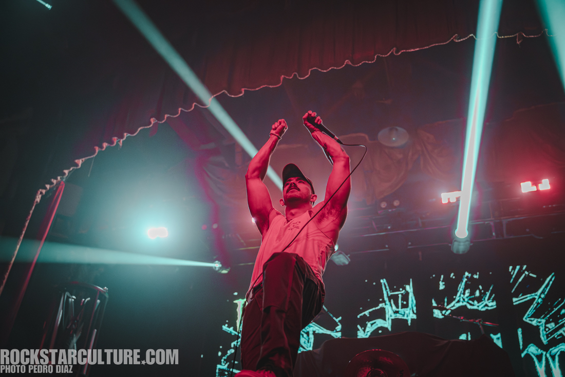 A musician performing on stage with a microphone, striking a dynamic pose under colorful stage lights.