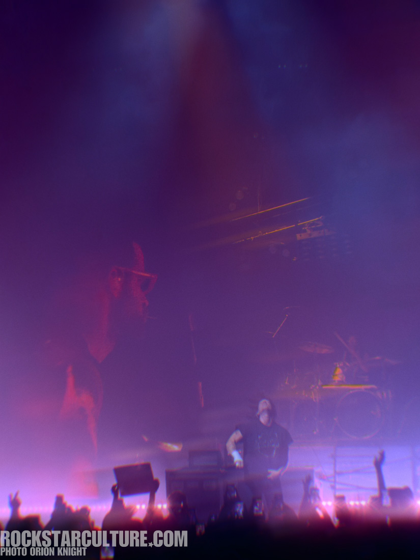 A musician performing on stage with colorful lighting and a blurred background, surrounded by an enthusiastic crowd holding up their phones.