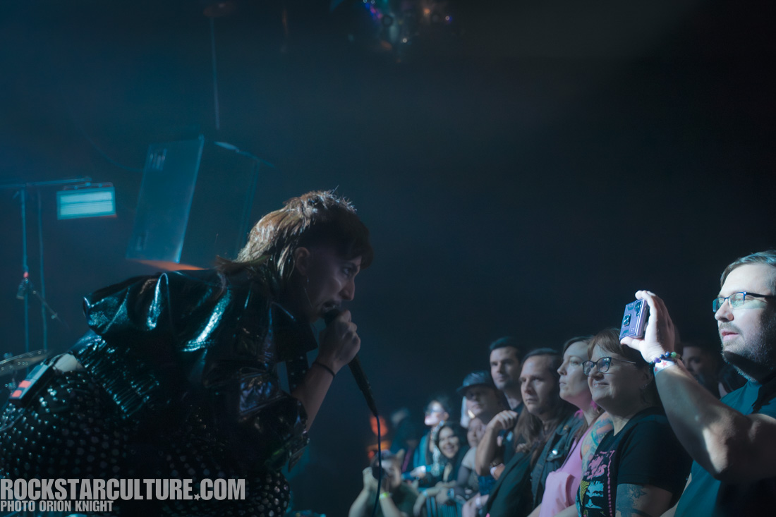 A vocalist performs passionately on stage, engaging with an audience, while fans eagerly watch and record the moment.