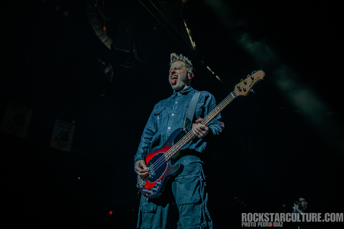 A musician performing on stage, passionately playing a bass guitar while making a dynamic expression.