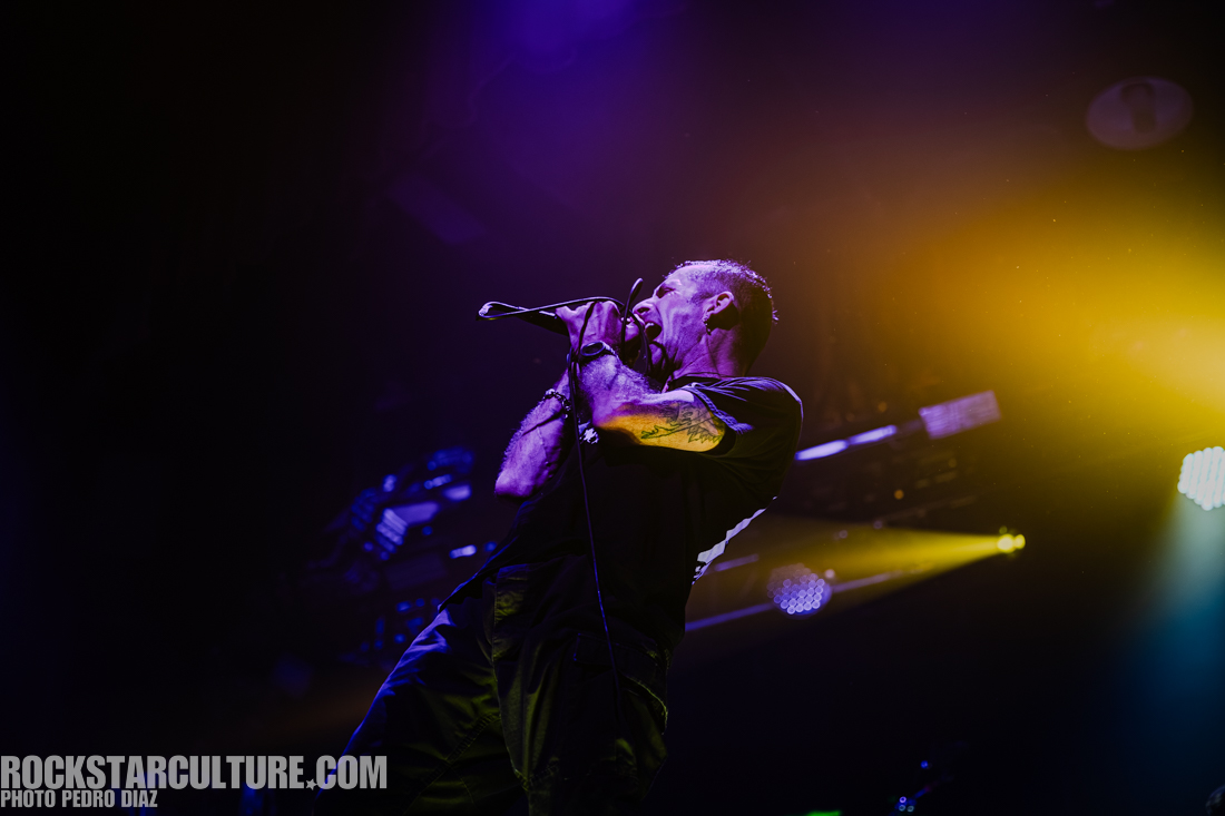 A male singer passionately performing on stage with a microphone, dramatic lighting in purple and yellow hues.