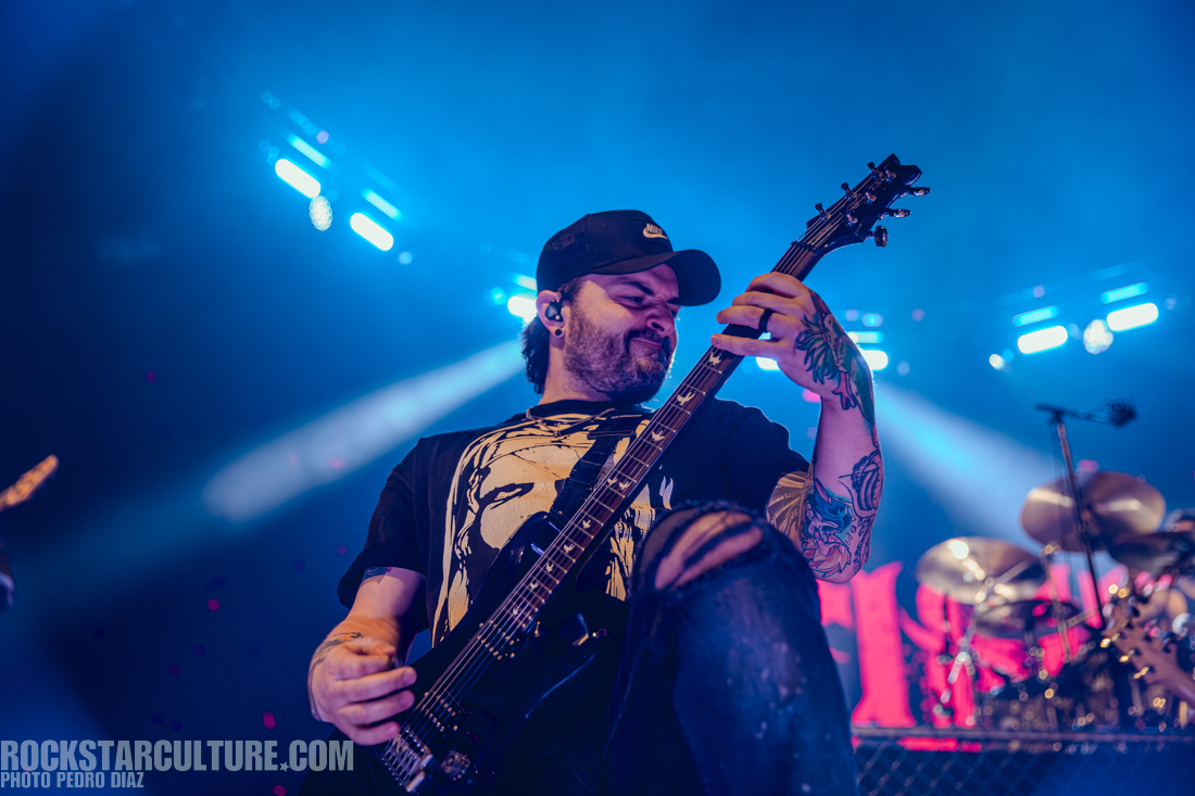 A guitarist passionately performing on stage with colorful lights in the background.