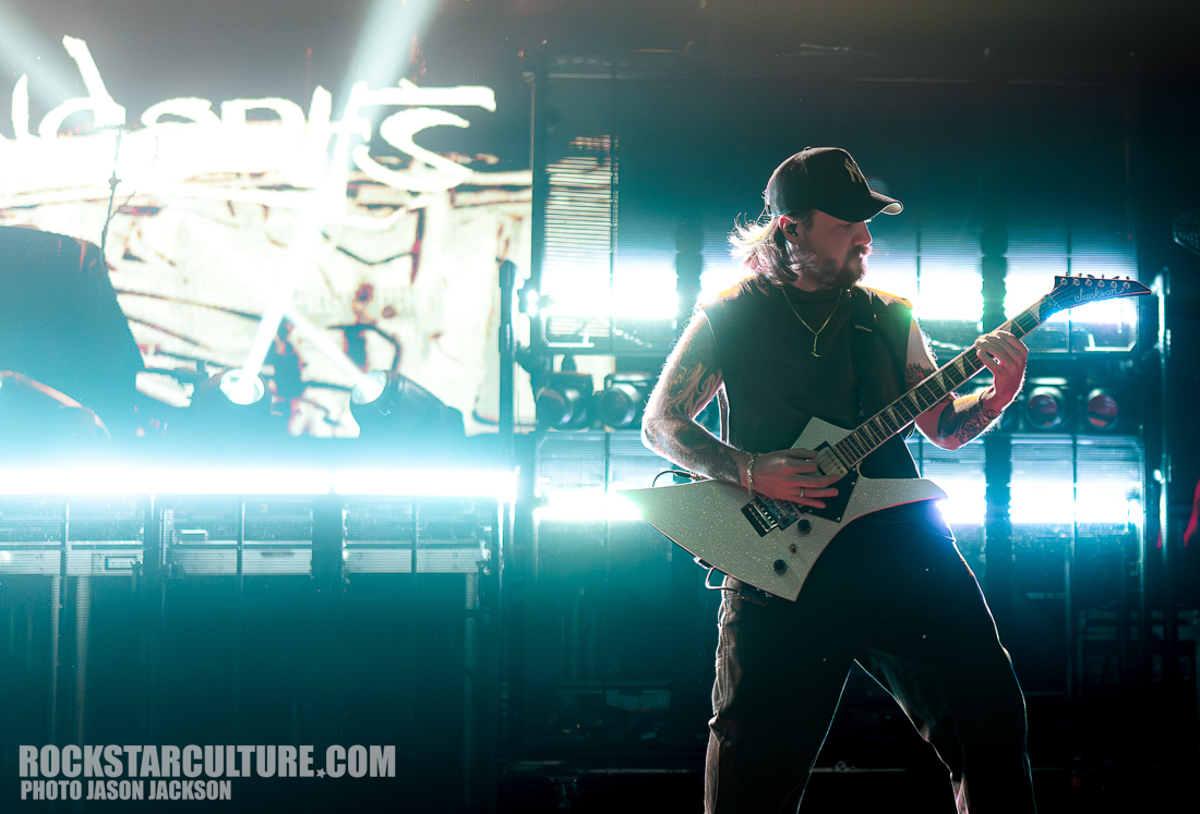 A guitarist performing on stage with dramatic lighting and a vibrant background.