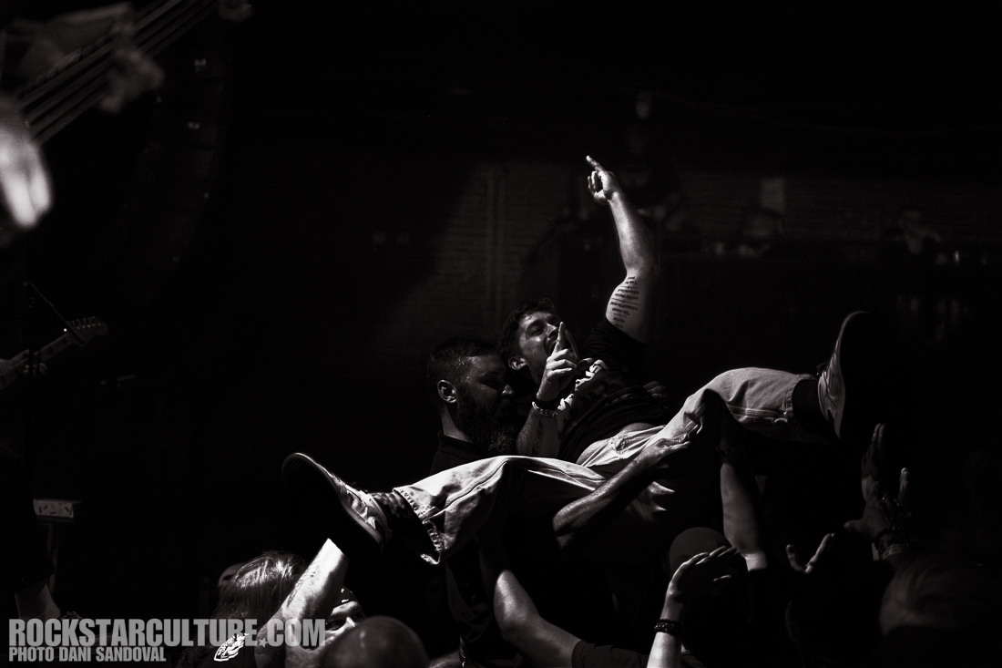 A crowd surfing individual is being supported by concert-goers during a live music performance, with a focus on the energy and excitement of the moment.