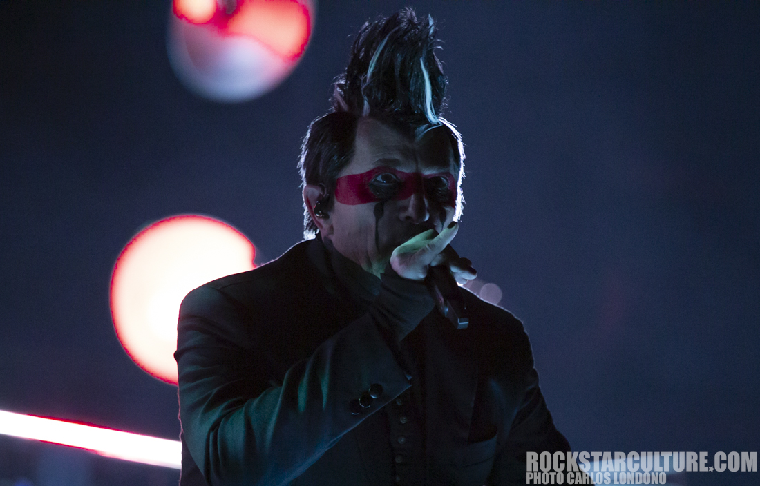 A singer performing on stage with dramatic lighting, wearing a black suit and striking red face paint.
