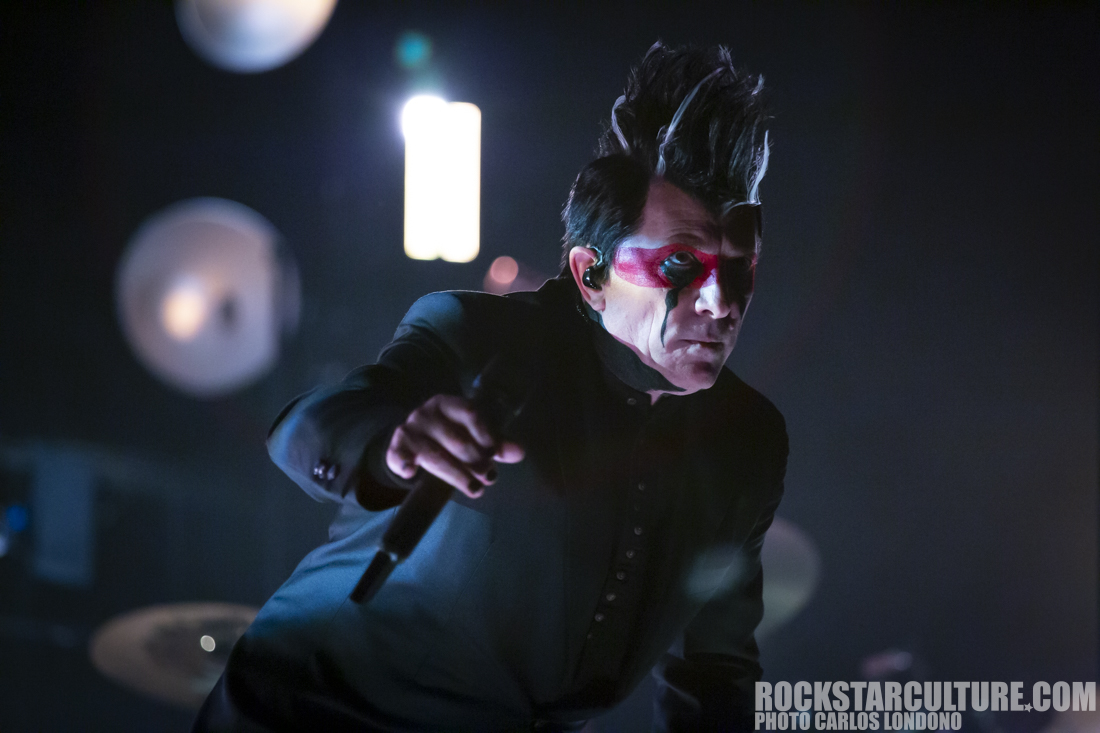 A performer on stage with striking makeup, including red face paint and a dramatic hairstyle, engaging with the audience during a concert.