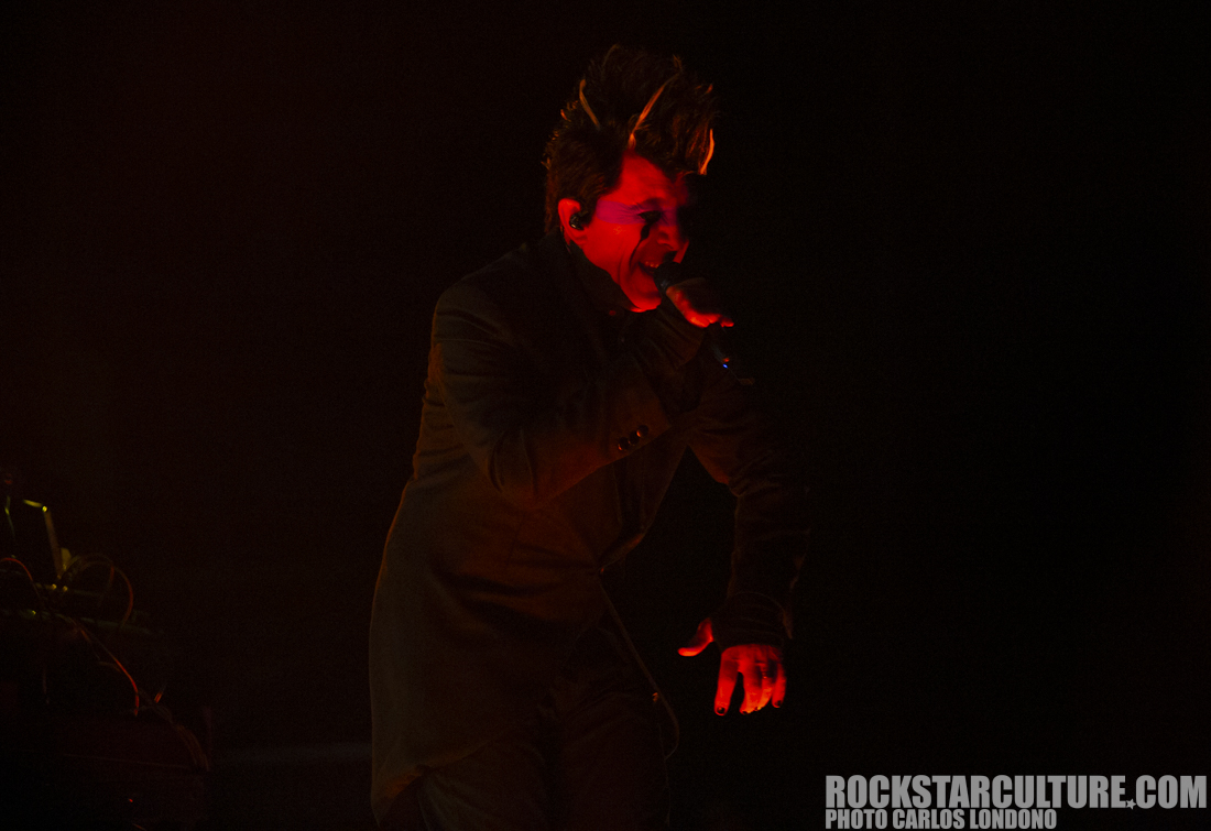 A musician passionately performing on stage, wearing a dark coat with dramatic lighting illuminating their face.
