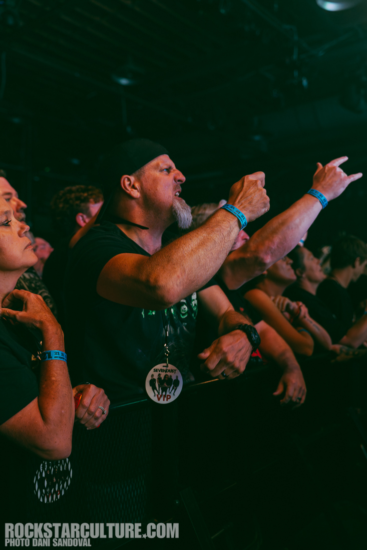 Audience members passionately enjoying a live music performance, with one man raising his hand and gesturing enthusiastically.