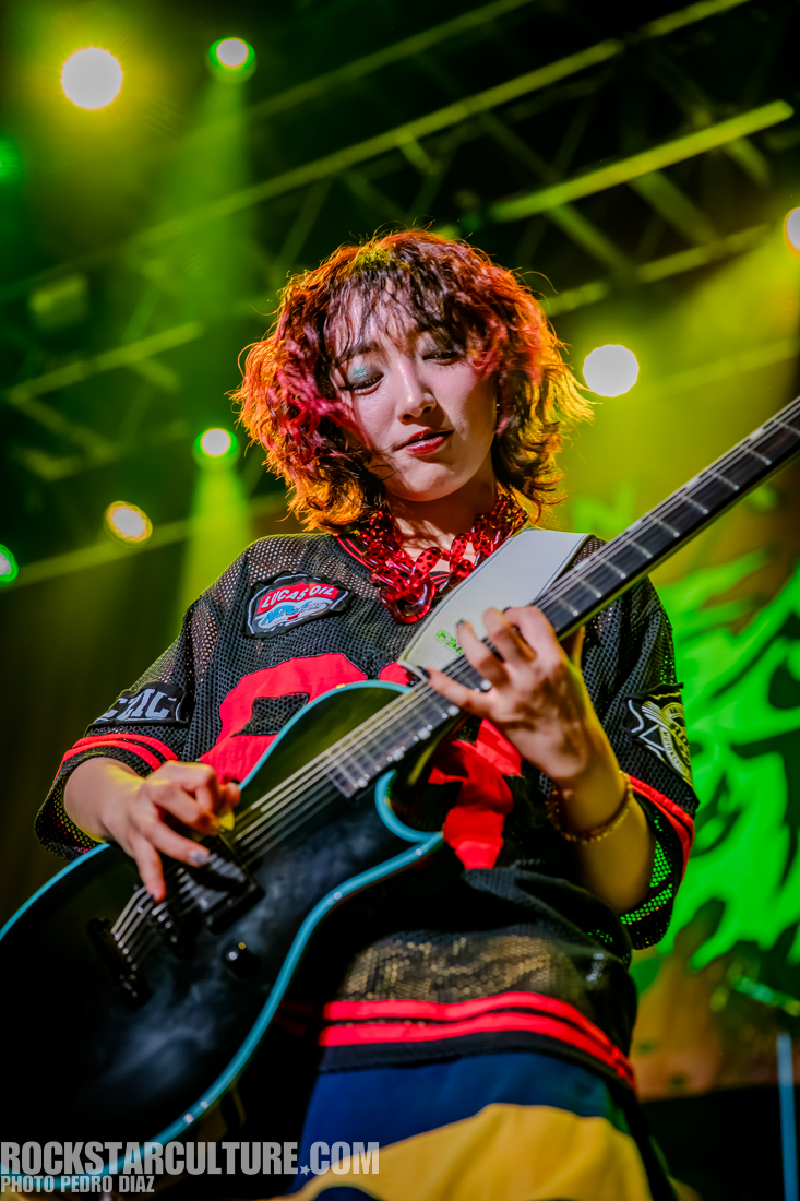 A musician passionately playing an electric guitar on stage with vibrant lighting in the background.