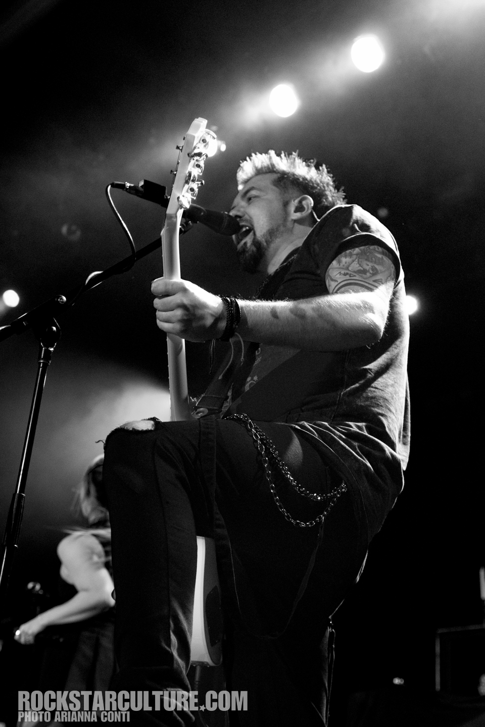 A musician performing on stage, passionately singing into a microphone while holding a white electric guitar, in black and white.