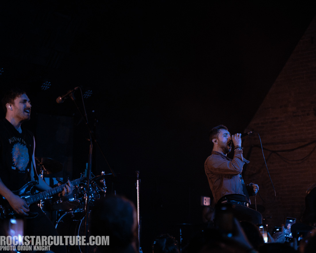 A rock band performing on stage, with the lead vocalist passionately singing into a microphone while the guitarist plays energetically.