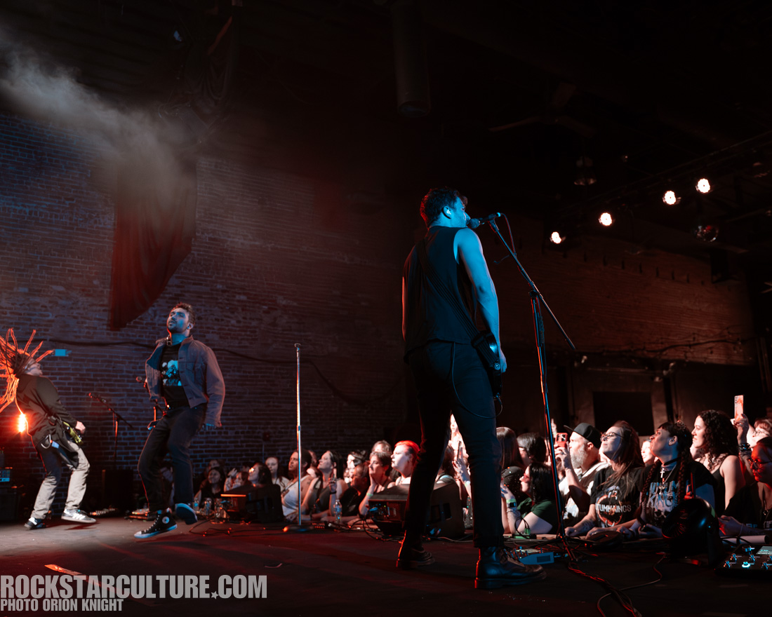 Band performing on stage with enthusiastic crowd in the foreground, dramatic lighting effects and a vibrant atmosphere.