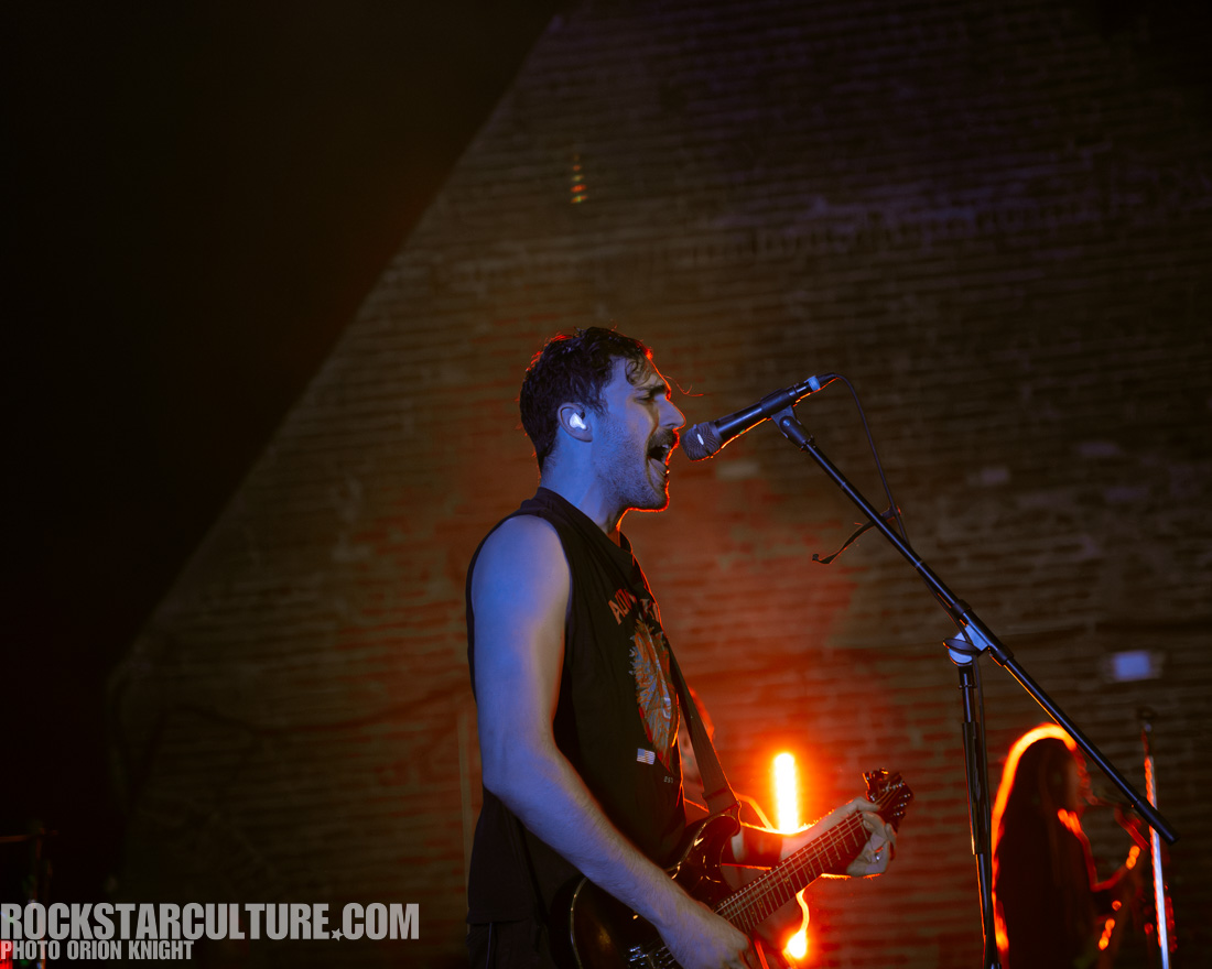 Male musician passionately performing on stage with a guitar and microphone, illuminated by vibrant stage lights.