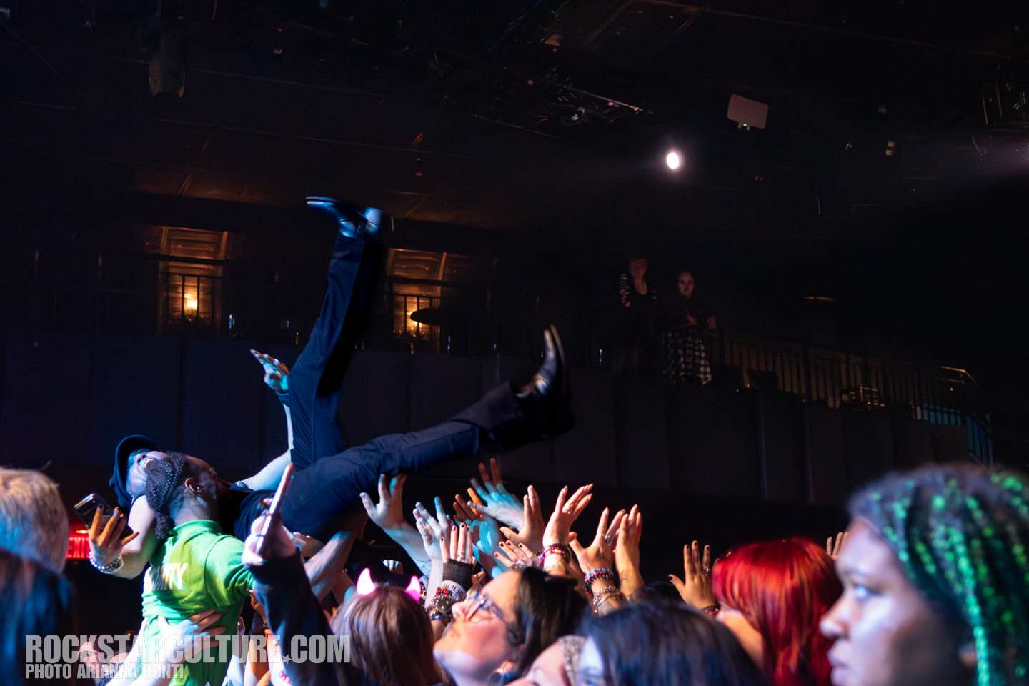 Crowd surfing performer above enthusiastic fans at a concert, with hands reaching up to catch him.