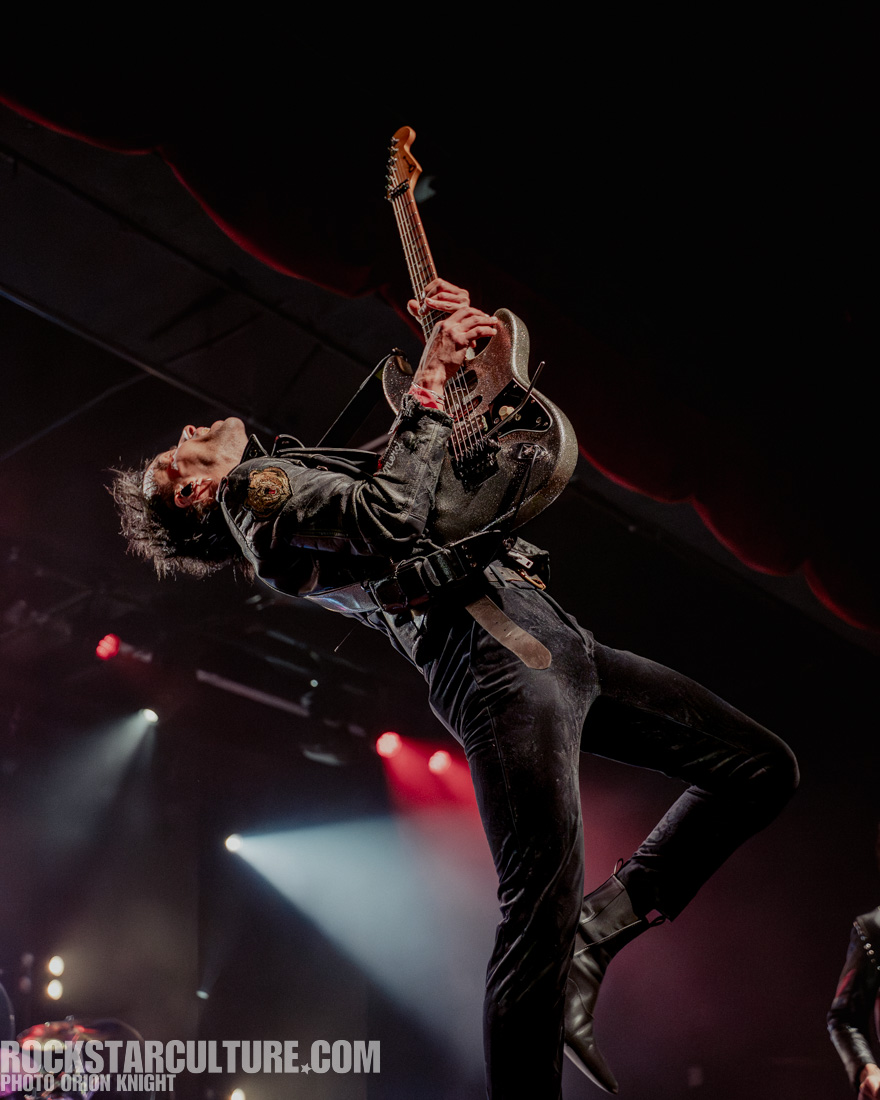 A guitarist performing on stage, leaning back while passionately playing an electric guitar. The scene is illuminated by stage lights, creating a vibrant atmosphere.