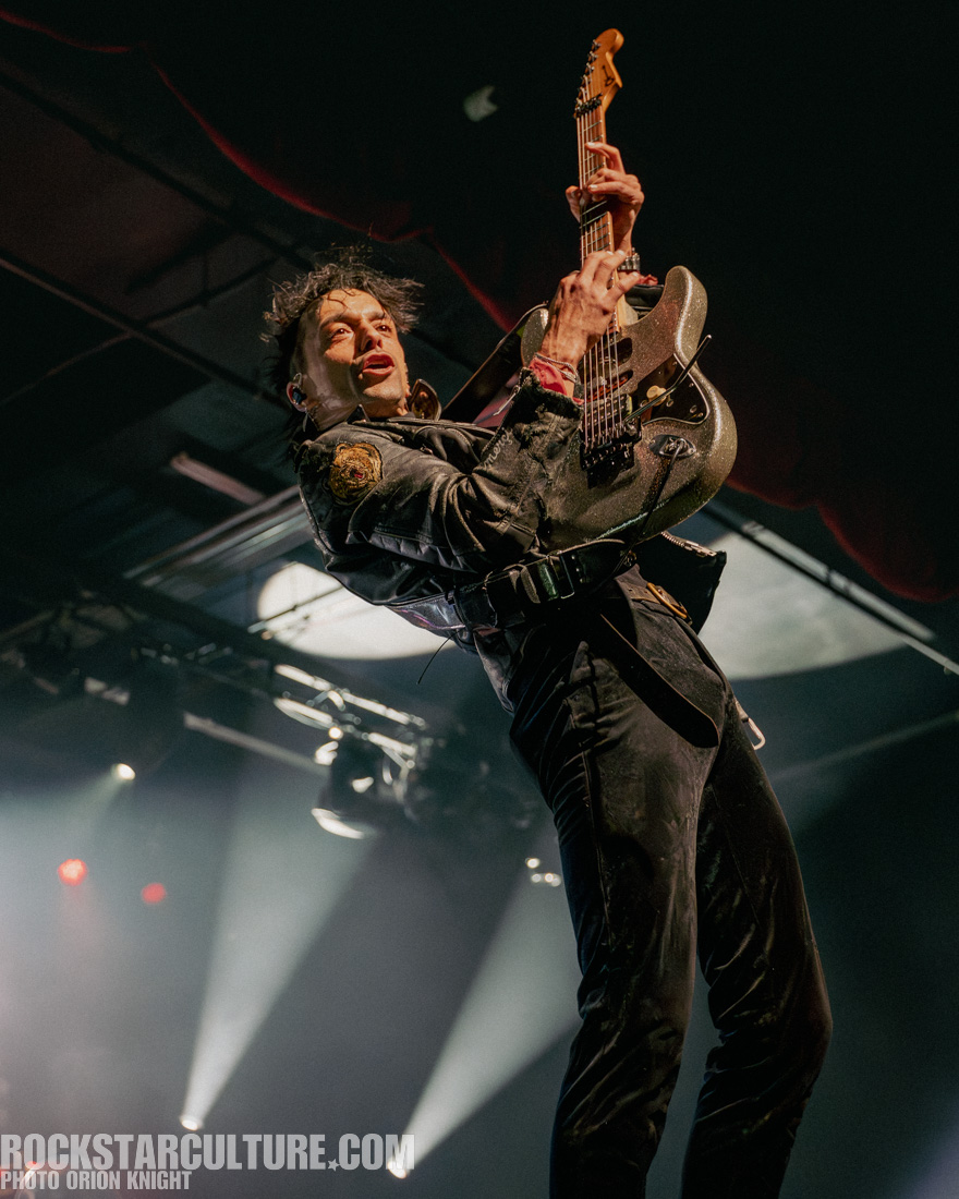 A musician passionately performing on stage with an electric guitar, wearing a black leather jacket and striking a dynamic pose amidst stage lights.