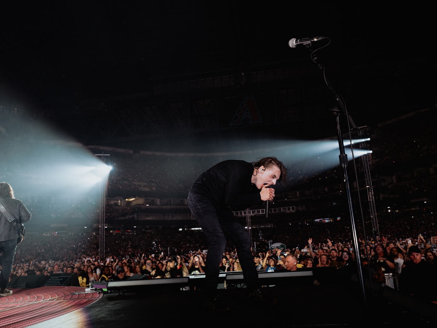 A singer passionately performing on stage in front of a large crowd, with dramatic lighting illuminating the scene.