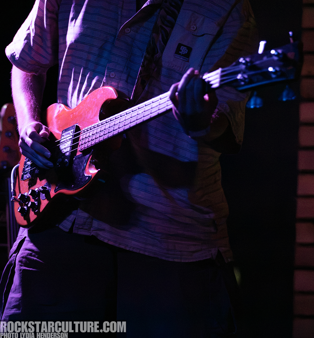 A musician playing an electric guitar on stage, illuminated by stage lighting.