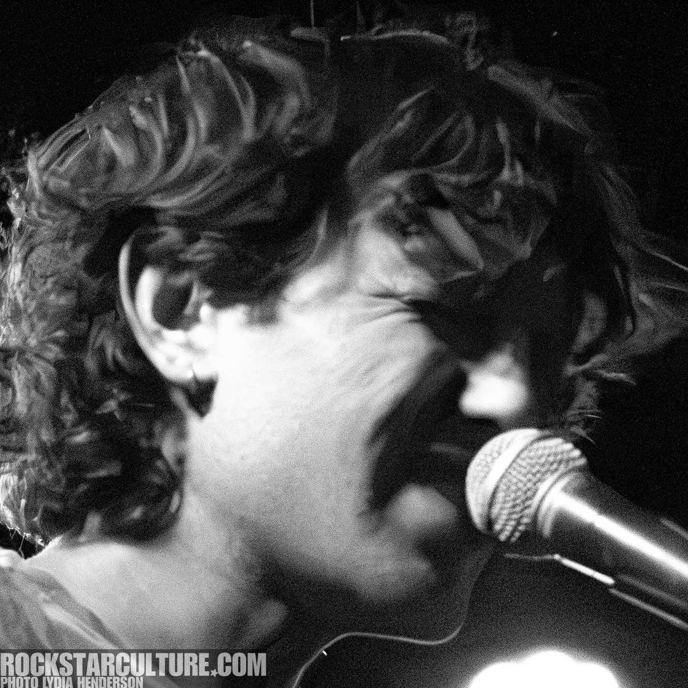 Black and white image of a singer passionately performing into a microphone with wavy hair.