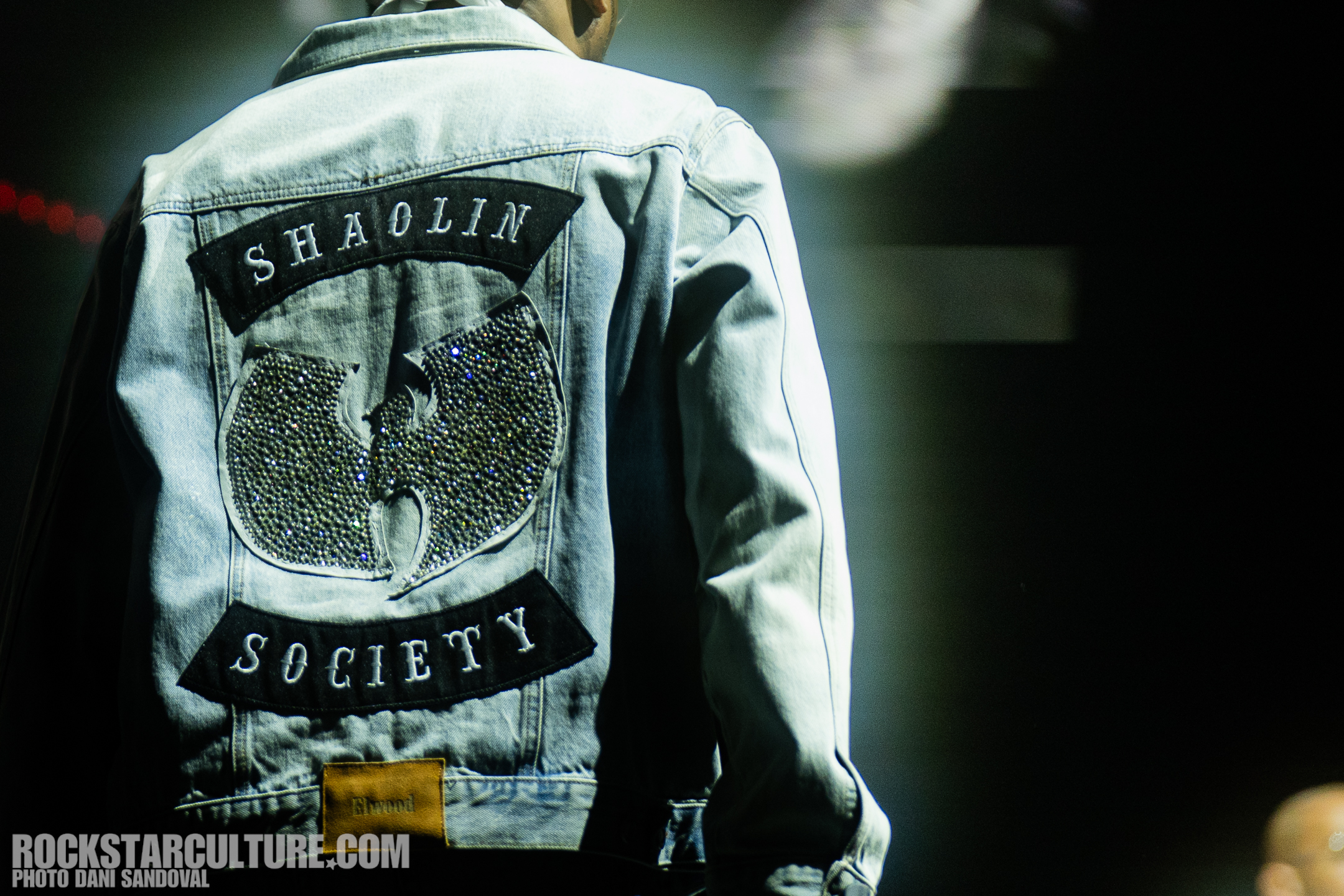 Person wearing a denim jacket with a Wu-Tang Clan Shaolin Society design on the back, captured in a performance setting.