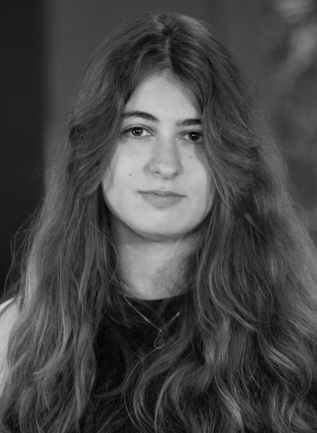 A black and white portrait of a young woman with long, wavy hair, looking directly at the camera.